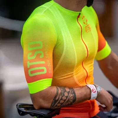 Camisola de ciclismo verde néon, laranja e vermelho com texto OTOSO THINK STRONG no braço