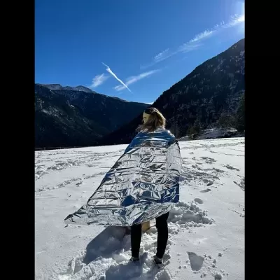 Mulher envolta em manta térmica prateada numa paisagem de neve com montanhas