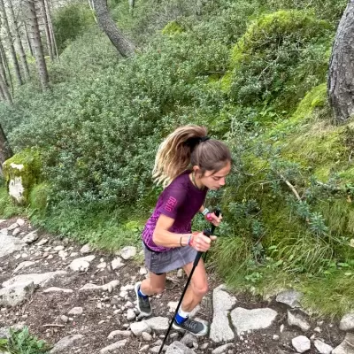 Mulher a caminhar em trilha pedregosa na floresta com bastões.
