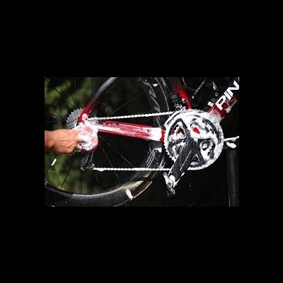 Bicicleta vermelha e preta com corrente sendo limpa por uma mão com pano branco