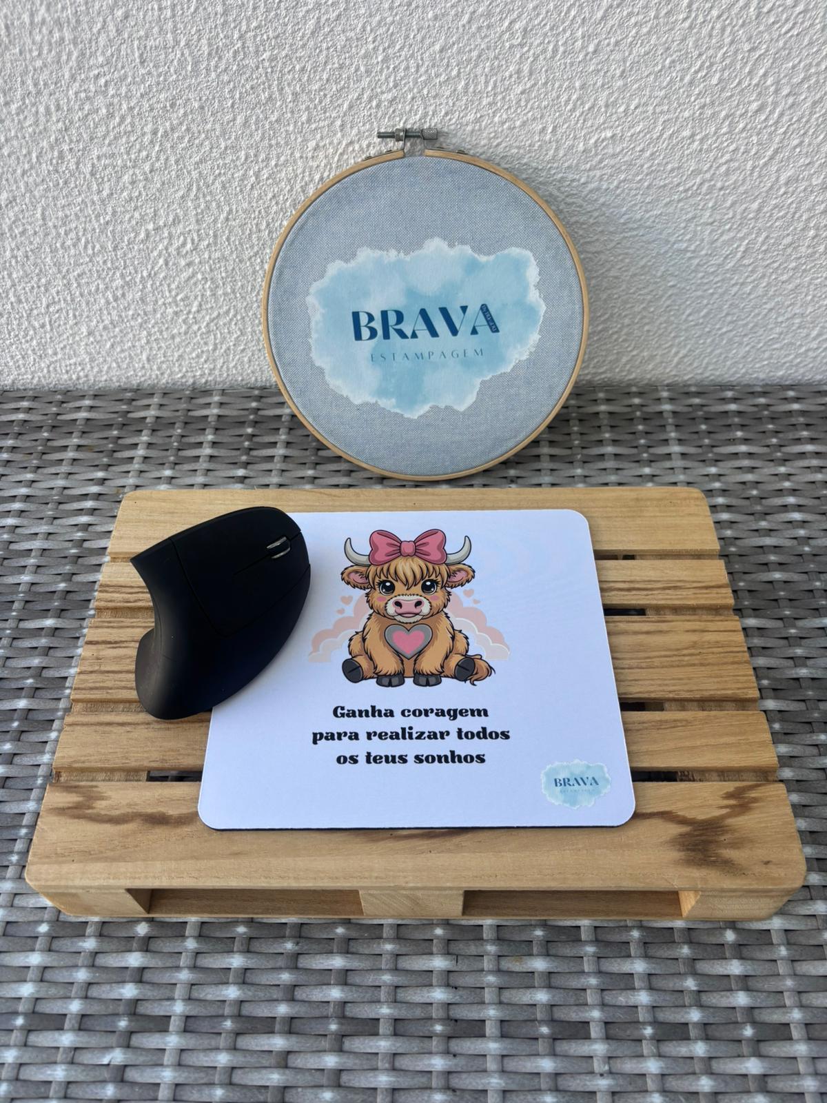 Base para Rato PC Mouse preto sobre tapete de rato com ilustração de vaca e texto motivacional em cima de suporte de madeira com bastidor ao fundo
