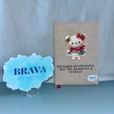 Caderno bege com urso e agradecimento para professora ao lado de placa azul com texto BRAVA ESTAMPA GEM