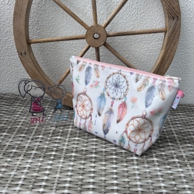 Necessaire com padrão de apanhadores de sonhos e fecho rosa colocada sobre superfície de rattan