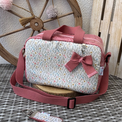 Mala pequena com padrão floral e alças rosa sobre mesa entre roda de madeira e móvel claro