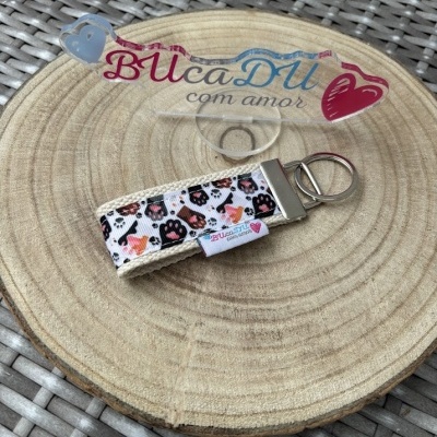 Chaveiro tecido com padrão de gatos e patas sobre base de madeira redonda