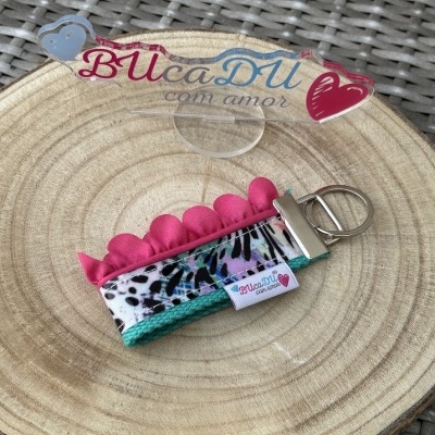 Chaveiro tecido colorido com padrão e etiqueta BUcaDU com amor sobre base de madeira redonda.