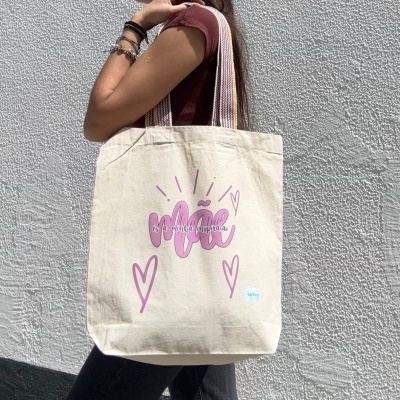 Mala tote bege em tecido com pega colorida, texto rosa e lilás, decorada com corações.