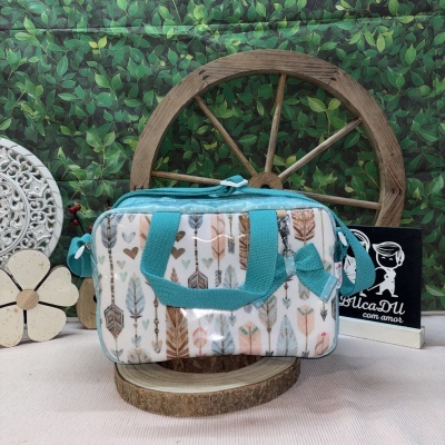 Bolsa estampada com penas e detalhes azuis, sobre base de madeira, fundo com folha verde e roda de madeira