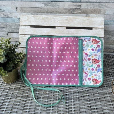 Estojo de tecido com padrão de estrelas e sereias coloridas aberto em superfície cinzenta trançada