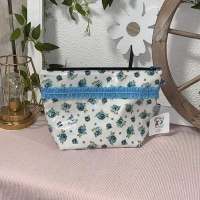 necessaire branca com flores azuis e fita azul sobre superfície rosa com decoração ao fundo