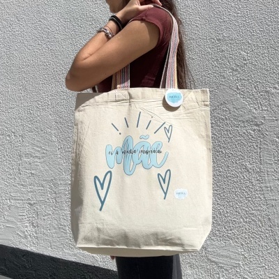 Mala tote bege com texto azul e alças coloridas.