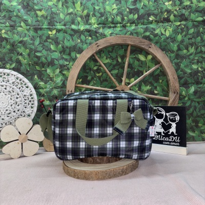 Bolsa quadrada xadrez verde e branco com laço e alças verdes em ambiente decorativo com fundo de folhas