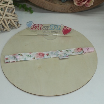 Fita para chupeta floral com fecho cor-de-rosa num suporte de madeira clara