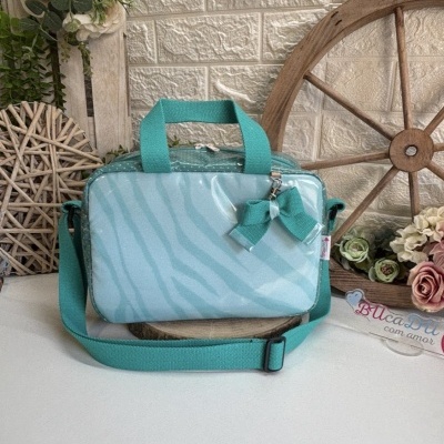 Mala azul-turquesa com alça e laço, em cenário com flores e roda de madeira