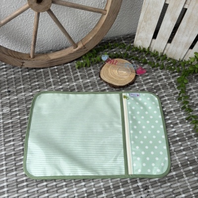 Bolsa verde com padrões de riscas e bolinhas, mesa de verga cinzenta e decoração de madeira e plantas.