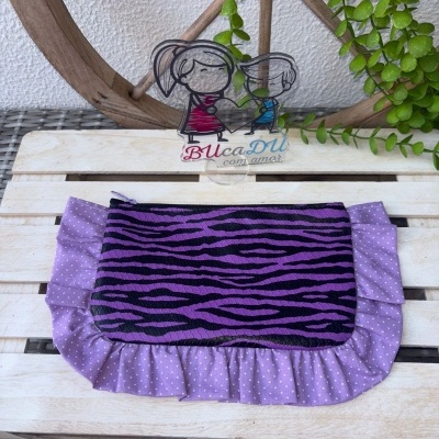 Bolsa padrão zebra roxa com remate lilás e bolinhas brancas sobre base de madeira clara.