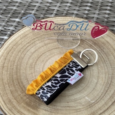 Chaveiro tecido padrão animal print preto branco com detalhe amarelo, argola metálica, etiqueta BUcaDU com amor, sobre base de madeira