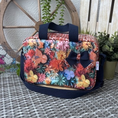 Bolsa colorida com padrão de flores e borboletas sobre mesa de rattan