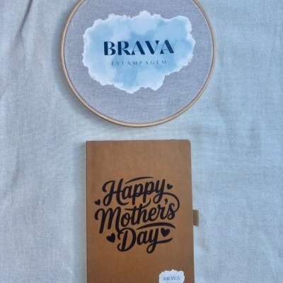 Caderno castanho com texto Happy Mothers Day e bastidor de madeira com tecido e logo BRAVA