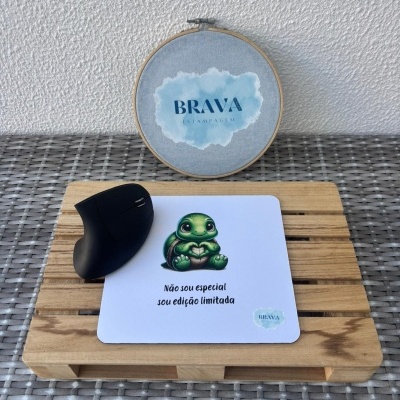 Tapete de rato branco com tartaruga e texto em português junto a rato preto ergonómico sobre base de madeira.