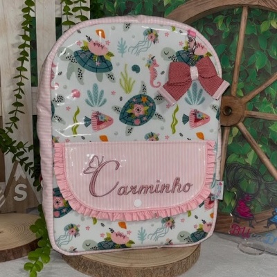 Mochila infantil colorida com estampado de tartarugas e bolso rosa com nome Carminho