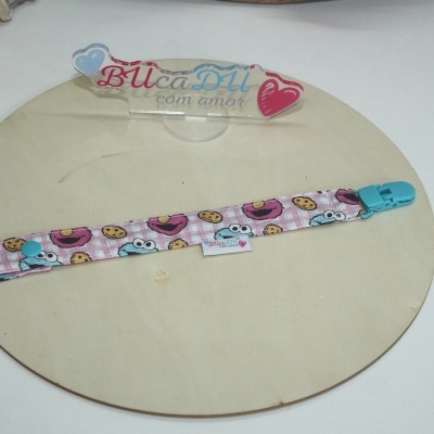 Gancho para chupeta com padrão colorido e clip azul sobre base de madeira com placa acrílica