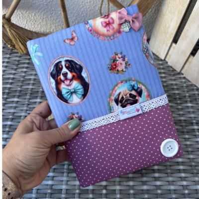 Capa de tecido azul com estampas de cães e elementos decorativos, parte inferior rosa com bolinhas e botão branco