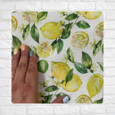 Tecido com padrão de limões e folhas verdes em fundo branco, mão com unhas coloridas tocando o tecido