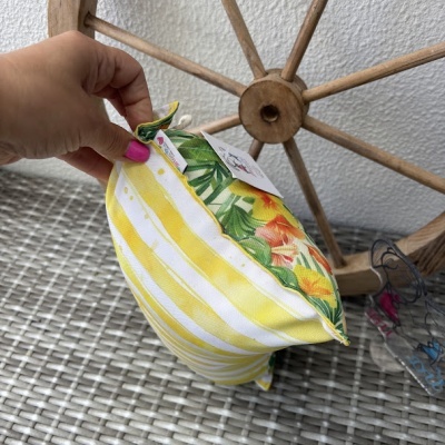 Almofada em tecido com riscas amarelas e brancas e estampa floral colorida, segurada por mão