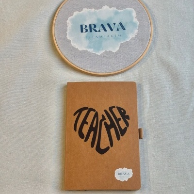 Caderno castanho com texto TEACHER em forma de coração e bastidor de bordado com logótipo BRAVA