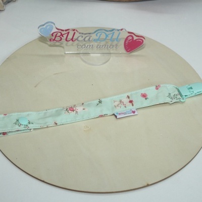 Fita verde-água com padrão de coelhos e flores, clip plástico e botão, sobre madeira redonda clara.