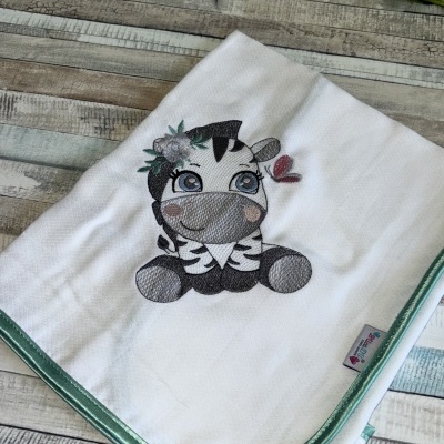 Fralda branca bordada com zebra e acabamento verde em superfície de madeira