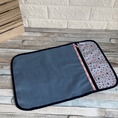 Capa de tecido azul com interior floral e fecho, em superfície de madeira