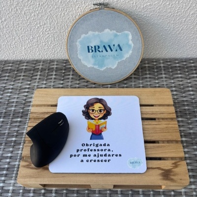 Rato de computador preto sobre tapete branco com ilustração e texto, base de madeira e bastidor com logo