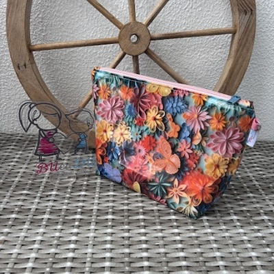 Necessaire colorida com padrão floral e borboletas sobre superfície de vime e roda de madeira ao fundo