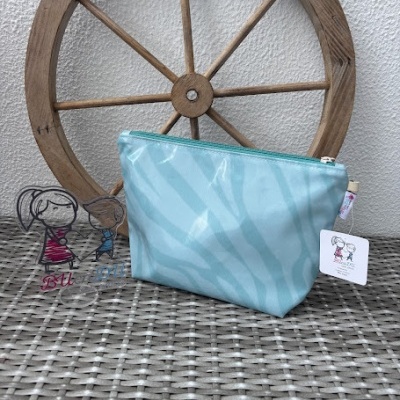 Necessaire azul claro com padrão zebra e fecho azul sobre superfície texturizada com roda de madeira ao fundo