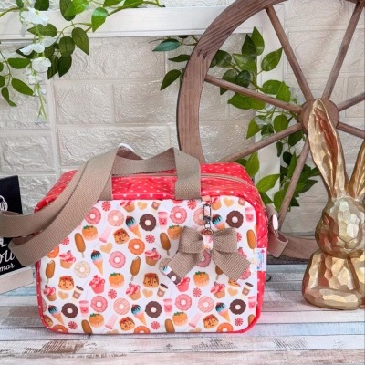 Mala pequena colorida com padrão de doces e detalhes vermelhos, com alça de tecido bege e laço pendurado.