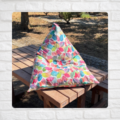 Pufe triangular colorido com padrão de folhas sobre mesa de madeira ao ar livre