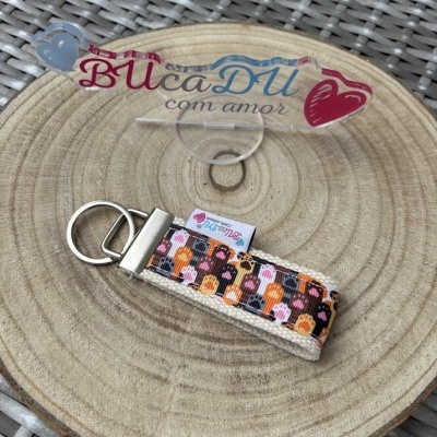 Chaveiro colorido com padrão de patas sobre suporte acrílico e tábua de madeira