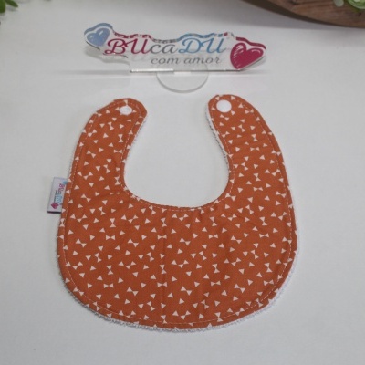 Babete laranja com padrão branco e fecho branco sobre fundo branco com decoração floral