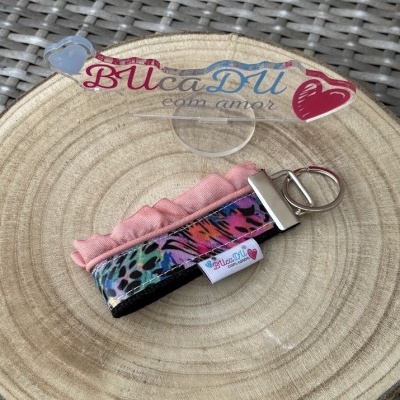 Chaveiro colorido com padrão animal, babado rosa, etiqueta BUcaDU com amor sobre madeira redonda e fundo de rattan