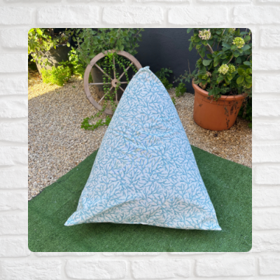 Pufe triangular com padrão azul e branco numa área exterior com plantas e carrinho de madeira.