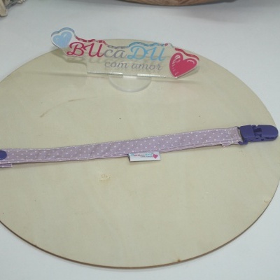 Fita lilás com padrões brancos e fecho roxo sobre placa redonda de madeira com autocolante BucaDU com amor