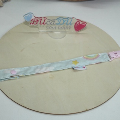 Fita para chupeta azul com padrão de nuvens e estrelas sobre suporte redondo de madeira