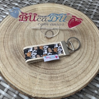 Chaveiro de tecido com padrão de vacas e suporte metálico sobre base de madeira