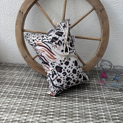 Travesseiro estampado animal print apoiado em roda de madeira sobre superfície cinza com bonecos de acrílico
