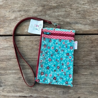 Bolsa pequena azul com padrão floral e fecho de correr vermelho sobre madeira rústica.