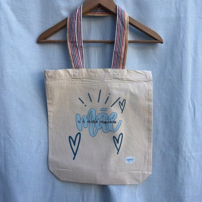 Saco de tecido bege com frase e corações, asas lisas coloridas, pendurado em cabide