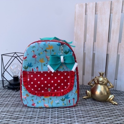 Mochila térmica colorida para criança com padrões de flamingos e bolso vermelho com bolinhas.