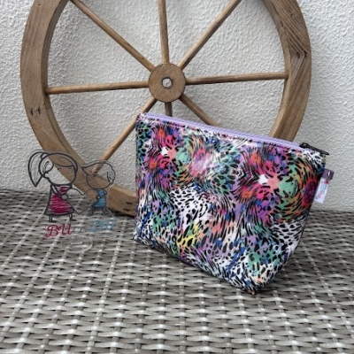 Bolsa colorida com padrão de manchas sobre mesa cinzenta com roda de madeira ao fundo